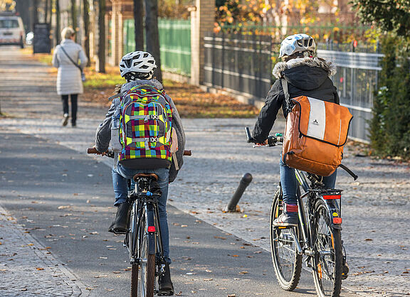 Zwei Kinder mit Rucksächen fahren auf einem baulich getrennten Radweg mit dem Fahrrad