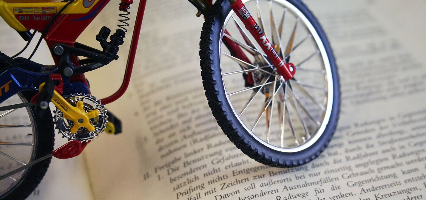Deutscher Gesetzestext mit Fahrradbezug Miniatur-Fahrrad steht auf einem aufgeschlagenen Buch mit deutschem Gesetzestext.